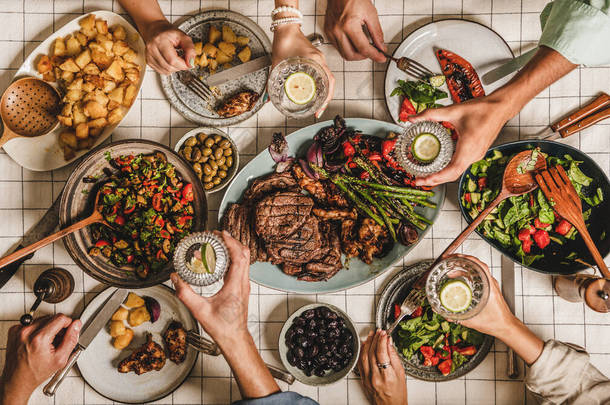 夏天的<strong>烤肉派对</strong>平铺的桌子，用<strong>烤肉</strong>，蔬菜，沙拉，烤土豆和人民的手与玻璃杯柠檬水覆盖在白色桌布，顶部视图。家庭团聚概念