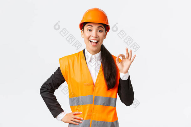 满意快乐的亚洲女工程师，戴着安全帽，身穿反光夹克的施工经理满意地展示出良好的姿态，保证了建筑的质量，确保了一切优秀