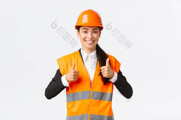 乐观的亚洲女建筑师给予许可，为结果感到自豪，戴着<strong>安全</strong>帽，身穿反思夹克，大拇指翘起表示赞许，保证了最佳的施工<strong>质量</strong>