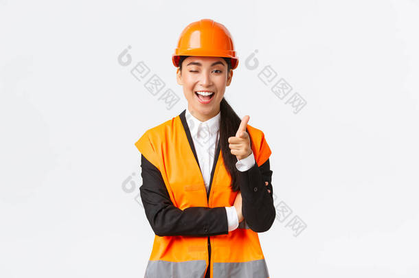 穿着安全帽和反光夹克，微笑专业的亚洲女施工经理，招揽新大楼的入住、眨眼和对着相机指指点点，向客户展示最佳地产