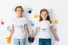 手里拿着颜料的快乐的孩子们，站在五颜六色的白色手印旁边 