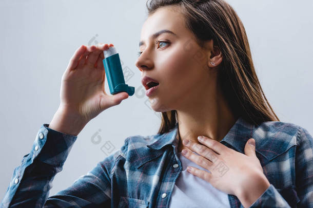 年轻的妇女使用哮喘<strong>吸入</strong>器和寻找离开隔离在灰色
