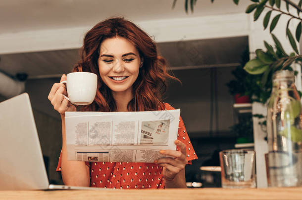 带咖啡的微笑的女人的肖像在桌子上<strong>看报</strong>纸在咖啡店的笔记本电脑