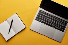 黄色表面上打开的笔记本电脑和笔记本电脑的顶部视图
