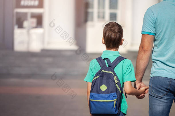 父亲带领一个小孩子上学的男孩手拉手。<strong>背后</strong>背着背包的父母和儿子