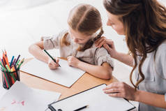 心理学家的高角度的看法与剪贴板坐在小孩附近, 而她用彩色铅笔画