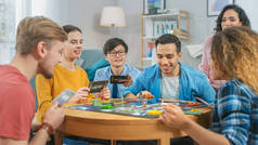 不同群体的男孩和女孩玩的战略棋盘游戏与卡和骰子。 白天舒适的客厅