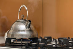 闪亮的不锈钢茶壶茶壶与开水在煤气炉上的厨房黄色复制空间背景.