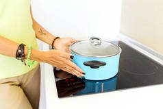厨房里的一位主妇在电磁炉上用特制的铁磁盘烹调食物。现代技术在家庭工作中的概念