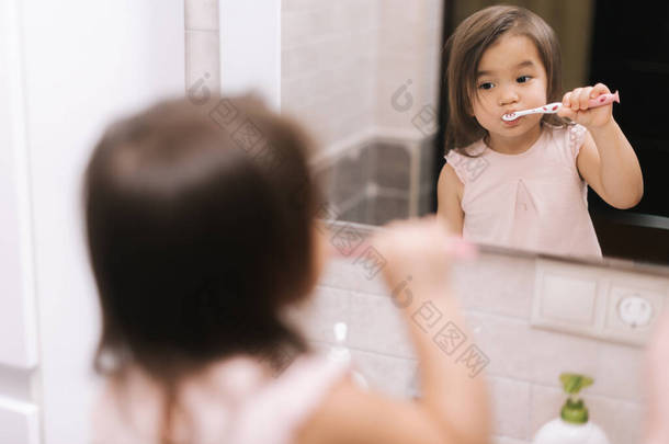 漂亮的小女孩正在浴室镜子前用牙刷刷牙