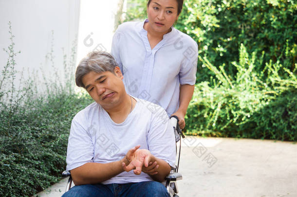 一个年长的亚洲;中年男子病人坐在轮椅上，他的妻子照顾他.健康与医学理念.