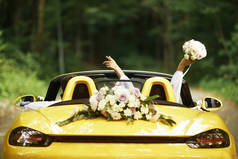 新婚夫妇带着结婚车。敞篷 车。后视图, 新娘举起她的手与花束.