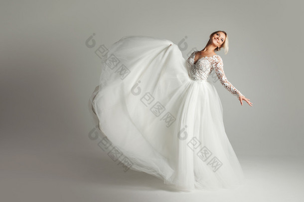 美丽的吸引力新娘穿着婚纱时有长时间充分的裙子，白色背景，跳舞和微笑