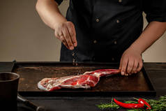 男厨师在木桌上用盐和胡椒擦生羊肉。厨师烹调羊肉开胃小腿.