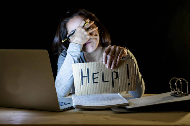 年轻疲倦和紧张的学生工作深夜在笔记本电脑持有帮助标志.