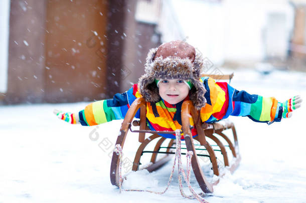小男孩喜欢在降雪时乘坐雪橇。坐着老式雪橇的学龄前儿童快乐.