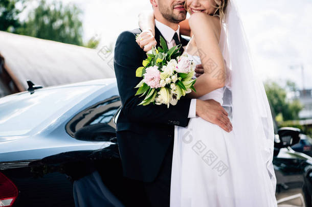 裁剪视图新郎在<strong>西装</strong>拥抱新娘在婚纱与花束