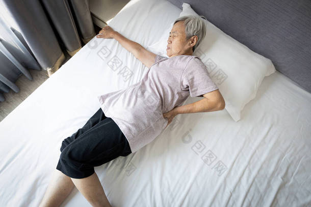 亚洲老年妇女睡觉时双手托着臀部或腰部，因肌肉发炎、背痛、老年人痛苦地试图从床垫上爬<strong>起来</strong>而痛苦的面部表情