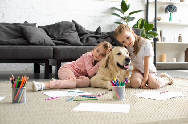 可爱的孩子抱着金色猎犬的狗, 而坐在地板上在家