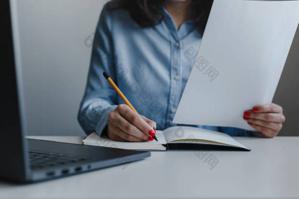 女人的手被红色的钉子包裹，用黄色铅笔写着便条，还拿着穿着蓝色衬衫的文件。商业，自由<strong>职业</strong>，自营<strong>职业</strong>。远程工作和在线工作概念