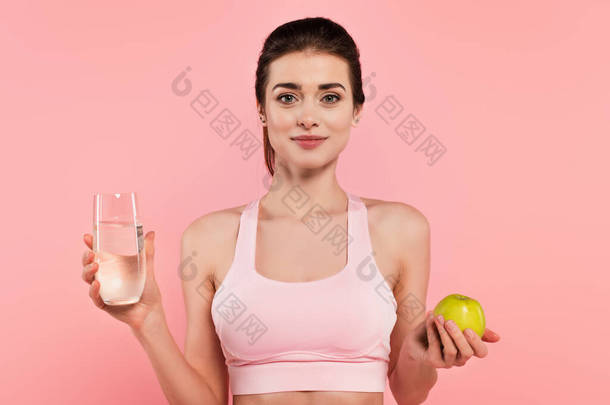 年轻的女运动员，手里拿着绿色的苹果和一杯粉红色的水 