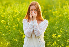 一个红头发的女孩对花粉和开花季节过敏，在花田里打喷嚏