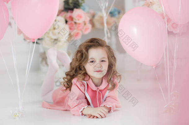 一个6岁的小女孩, 长卷发, 穿着粉红色的连衣裙和白色的紧身衣, 一个美丽的微笑, 独自坐在一个大明亮的房间, 有很多粉红色的气球, 在心脏的形状。情人节和聚会庆典.