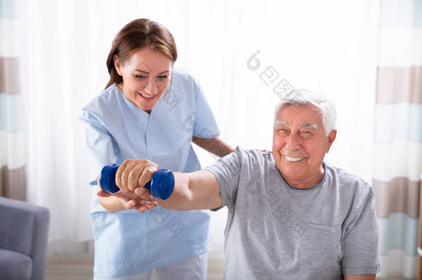 年轻的女护士帮助快乐的老年男子做哑铃运动
