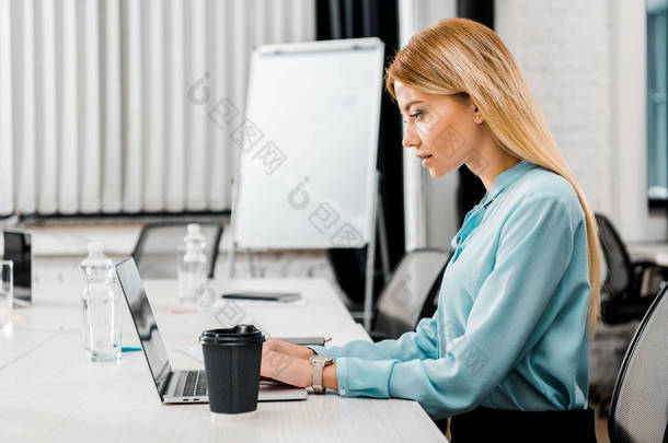在办公室里工作的笔记本电脑上工作的重点女商人的侧视图