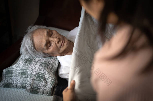 亚洲老年妇女睡在卧室的床上，女护理人员用毛毯盖住老年病人，帮助老年人，在养老院为老年人铺毛毯，提供帮助、照顾、支持 