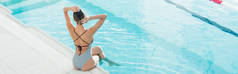 坐在温泉中心游泳池边，穿着泳衣调整头发的女人的背影，横幅