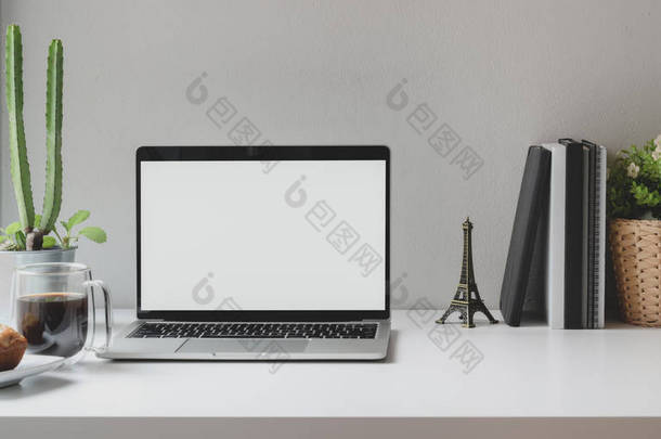 靠窗的舒适工作环境，配有装有咖啡杯和办公用品的开放式空白屏幕笔记本电脑 