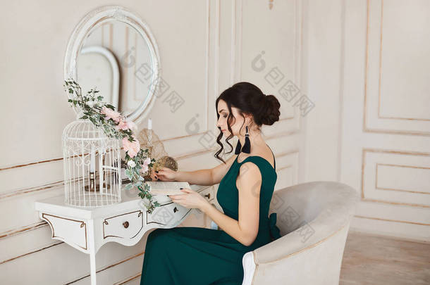 时尚黑发女人与时尚的发型在时尚的晚礼服和时尚的鞋子坐在梳妆台