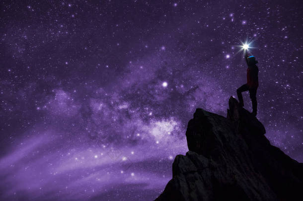 登山者或背包客的剪影, 他把明星高高举起头顶。站在岩石山峰上对抗银河系, 恒星和太空尘埃在宇宙中, 成功, 领导概念.