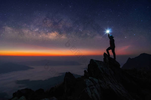 登山者或背包客剪影。在他的手里, 他把灯高高地举在头顶上。站在落基山脉山顶和银河, 成功, 赢家, 领导理念。高 iso 噪声.