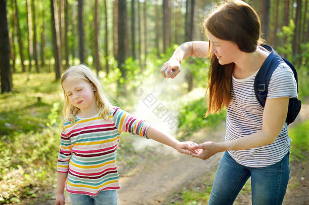 妈妈在森林徒步旅行美丽的<strong>夏</strong>日前对女儿施用驱虫药。在<strong>夏</strong>天保护孩子们<strong>不</strong>咬昆虫.用喷雾器与孩子的积极闲暇.