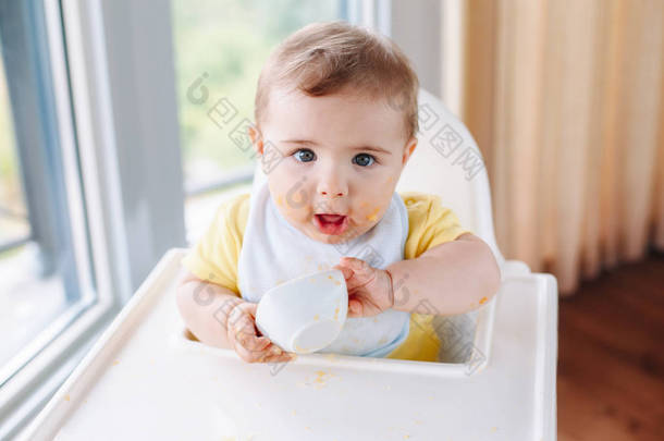可爱可爱的白人孩子的肖像, 肮脏的凌乱的脸坐在高高的椅子上吃苹果泥用手指。每天家庭的童年生活。婴儿<strong>尝试</strong>补充婴儿食品