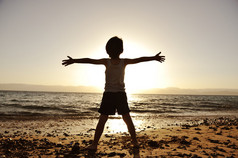 孩子在沙滩上举起他的手，朝着太阳的剪影