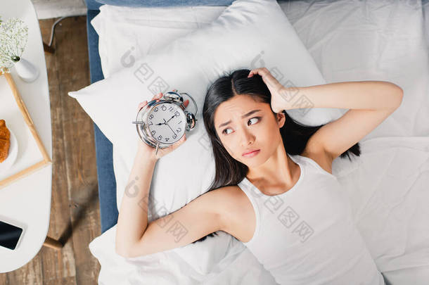 上午忧心忡忡的亚洲女人抱着闹钟躺在床上的头像 