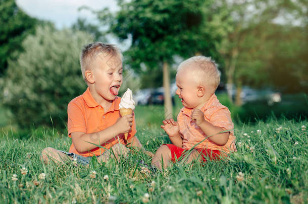 两个白人有趣的孩子男孩<strong>兄弟</strong>姐妹坐在一起吃共享一个冰淇淋。蹒跚学步的婴儿在哭，哥哥在戏弄他。爱羡慕嫉妒<strong>兄弟</strong>友谊.
