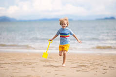 孩子们在热带海滩上玩耍。一个拿着铲子和铲子的小男孩在海滨.家庭暑假。孩子们在建造沙堡水和沙子对孩子们来说很有趣.孩子们玩，在海滨建造城堡
