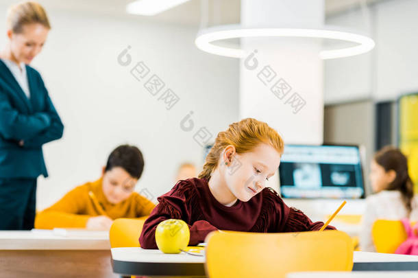 老师看着可爱的学童在<strong>课桌</strong>上写作和学习