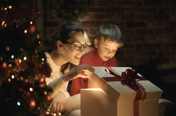 快乐的男孩和他的母亲在家里<strong>打开一个</strong>神奇的圣诞礼物, 圣诞树在前景: 假期和家庭<strong>概念</strong>
