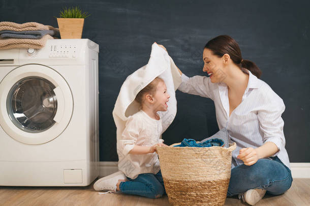 在家里洗衣服的时候，漂亮的年轻妇女和小女孩的小助手们都在开心地笑着.                                
