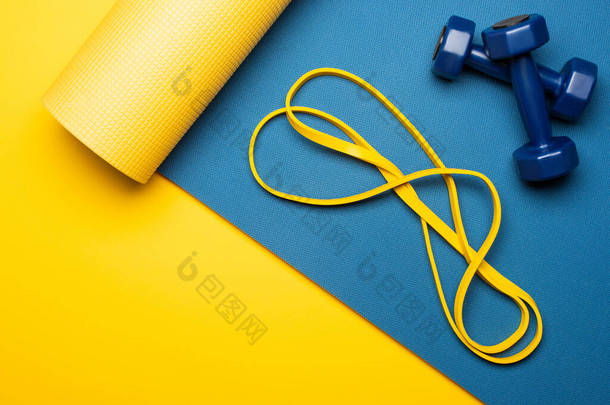 带黄色背景哑铃和电阻带的蓝色健身垫顶部视图
