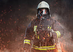 一名职业消防员身着制服和氧气面罩站在火灾火花和烟雾在黑暗的背景下.