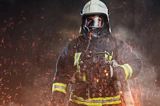 一名职业消防员身着制服和<strong>氧气</strong>面罩站在火灾火花和烟雾在黑暗的背景下.