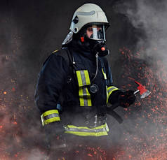 一名身穿制服和氧气面罩的消防员手持一把红色斧头站在火的火花和烟雾在黑暗的背景.