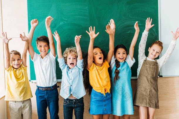 可爱的快乐学童举起双手站在空白黑板前