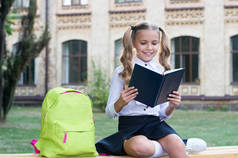 在校女生可爱的孩子背着背包在户外放松一下，看书的概念